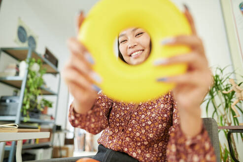 Lächelnde Geschäftsfrau schaut durch Ringspielzeug im Büro - KIJF04230