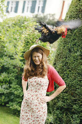 Rooster flying over woman's head in garden - AANF00135