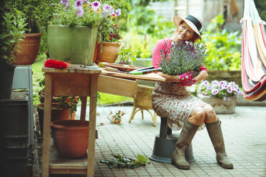 Lächelnde Frau träumt, während sie eine Lavendelpflanze im Hinterhof hält - AANF00139