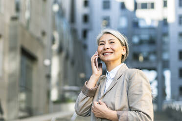 Lächelnde Frau, die in der Stadt mit einem Smartphone telefoniert - OIPF01362