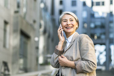 Glückliche reife Frau, die in der Stadt mit einem Smartphone telefoniert - OIPF01364