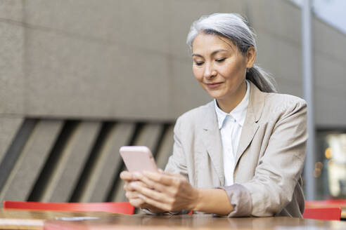 Mature woman text messaging through smart phone at sidewalk cafe - OIPF01370