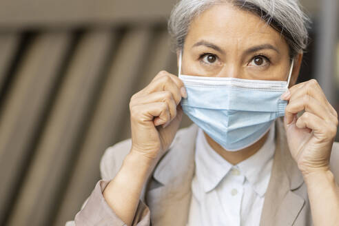 Woman adjusting protective face mask during COVID-19 - OIPF01376