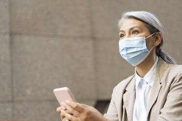 Woman with gray hair holding smart phone during pandemic - OIPF01379