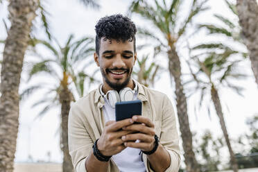 Smiling young man with black hair using smart phone - XLGF02350