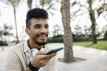 Man with wireless headphones sending voicemail through smart phone - XLGF02351