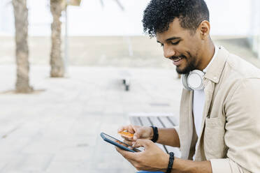 Lächelnder Mann, der eine Kreditkarte hält und mit einem Smartphone bezahlt - XLGF02355