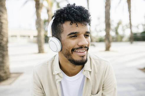 Lächelnder junger Mann hört Musik über drahtlose Kopfhörer - XLGF02356