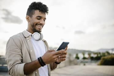 Happy man with wireless headphones using smart phone - XLGF02388