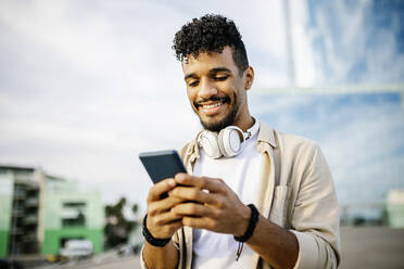 Glücklicher Mann mit Kopfhörern und Smartphone - XLGF02390