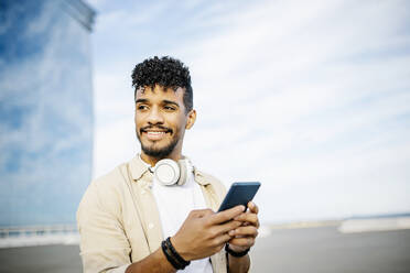 Smiling man with black curly hair holding smart phone - XLGF02391