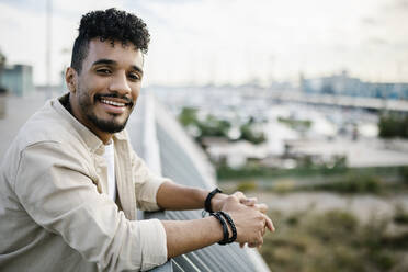 Lächelnder junger bärtiger Mann auf der Terrasse eines Gebäudes - XLGF02393