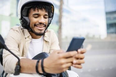 Smiling man wearing crash helmet using mobile phone - XLGF02396