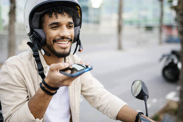 Man wearing crash helmet sending voicemail through smart phone - XLGF02397