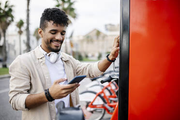 Smiling man using mobile phone at bicycle parking station - XLGF02399