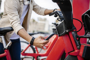 Man unlocking bicycle through smart phone at parking station - XLGF02400