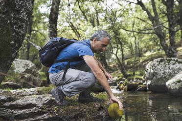 Mature man filling water in bottle at pond during vacation - JCCMF04236