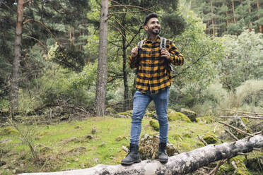 Lächelnder mittelgroßer erwachsener Mann auf einem Baumstamm im Wald stehend - JCCMF04242