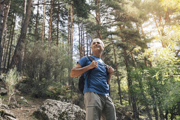 Lächelnder männlicher Tourist mit Rucksack im Wald stehend im Urlaub - JCCMF04249
