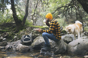 Mann mit Strickmütze trinkt Kaffee mit Hund im Wald - JCCMF04252