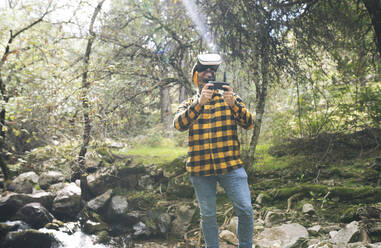 Smiling man using virtual reality simulator in forest - JCCMF04254