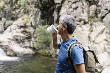 Mature man drinking coffee by pond - JCCMF04267