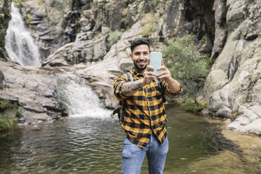 Smiling mid adult man taking selfie through smart phone by pond in forest - JCCMF04271