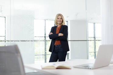 Confident businesswoman standing with arms crossed in office - FKF04372