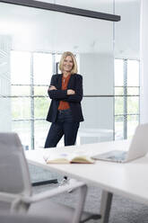 Smiling businesswoman standing with arms crossed in office - FKF04377