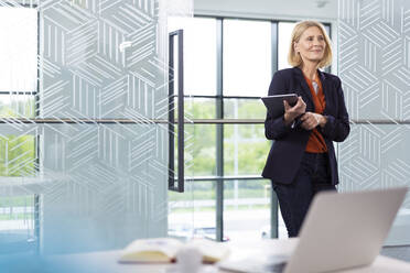 Reife Frau mit blondem Haar hält digitales Tablet im Büro - FKF04394