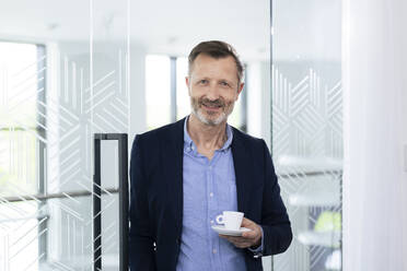 Smiling male professional holding coffee cup in office - FKF04399