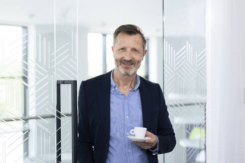 Lächelnde männliche Fachkraft hält Kaffeetasse im Büro - FKF04399