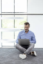 Businessman using laptop while sitting on ground in corridor - FKF04423