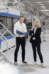 Businessman discussing strategy with female colleague in factory - FKF04429