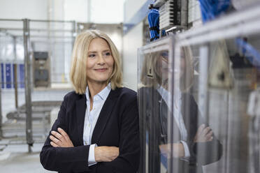 Smiling female professional with arms crossed standing by machinery in industry - FKF04478