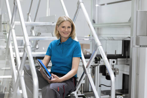 Lächelnde Frau, die ein digitales Tablet hält, während sie auf einer Treppe sitzt - FKF04492