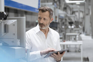 Businessman holding digital tablet while looking at machinery in factory - FKF04506