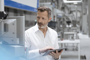 Geschäftsmann hält digitales Tablet und betrachtet Maschinen in einer Fabrik - FKF04506