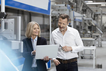 Smiling businesswoman explaining business strategy over laptop to male colleague in factory - FKF04508