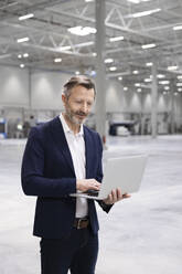 Businessman using laptop while standing in industry - FKF04532