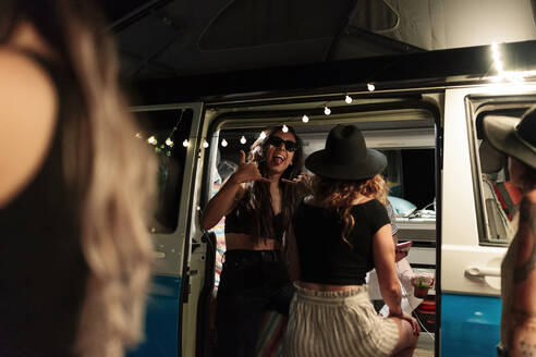 Woman showing shaka sign during party with female friends in camper van - MRRF01603