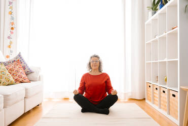Senior woman meditating while sitting cross-legged at home - GPF00069