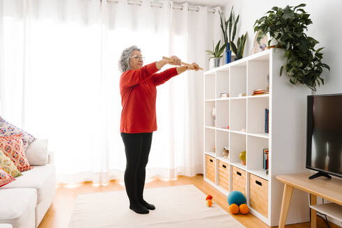 Frau, die einen Stock hält, während sie zu Hause gymnastische Übungen macht - GPF00075