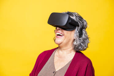 Ältere Frau lacht, während sie ein Virtual-Reality-Headset vor gelbem Hintergrund trägt - GPF00082