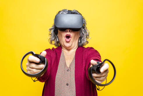 Frau spielt ein Videospiel auf einem Virtual-Reality-Headset und hält einen Joystick vor einem gelben Hintergrund - GPF00087