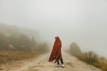 Young man covered in blanket standing on road - ACPF01370