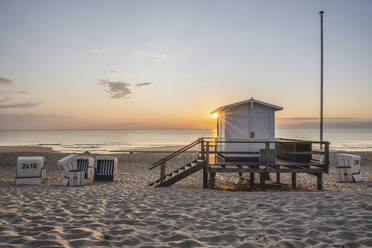 Lifeguard hut and hooded beach chairs at sandy coastal beach during sunset - KEBF02030