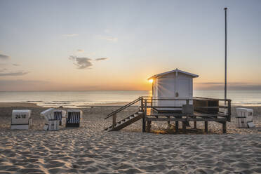 Rettungsschwimmerhütte und Strandkörbe mit Kapuze am sandigen Küstenstrand bei Sonnenuntergang - KEBF02030