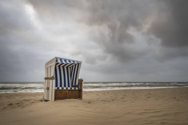 Sturmwolken über einem einsamen Strandkorb mit Kapuze an einem leeren Strand - KEBF02044