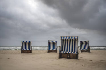 Storm clouds over hooded beach chairs standing on empty beach - KEBF02045